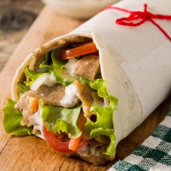 A Kabob Zone kebab wrap, filled with meat, lettuce, tomatoes, and white sauce, tied with red string.