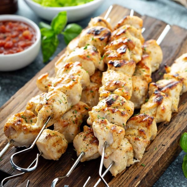 Grilled chicken shish kebabs on skewers, garnished with herbs, served on a wooden board.