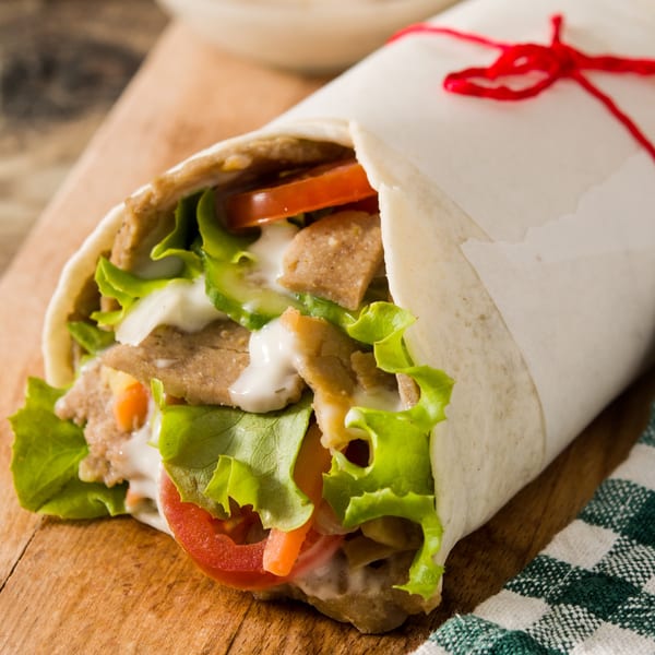 A Kabob Zone kebab wrap, filled with meat, lettuce, tomatoes, and white sauce, tied with red string.