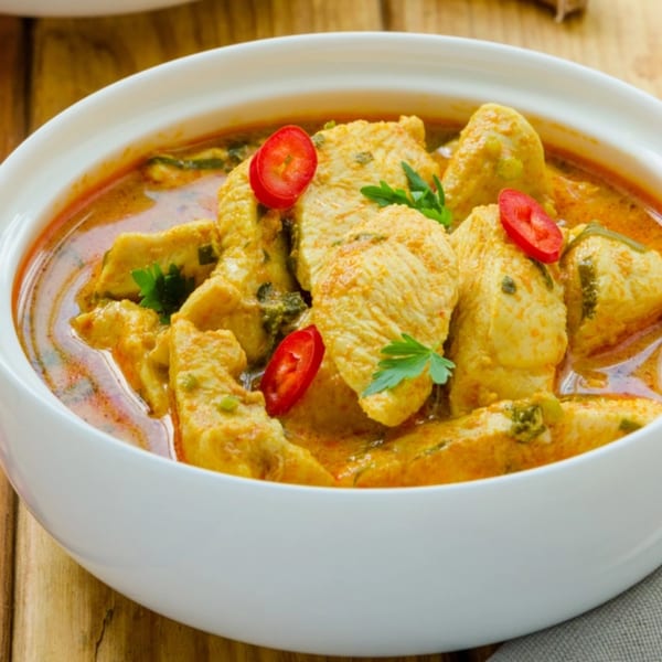 Chicken curry with red chili slices and parsley in a white bowl on a wooden table.