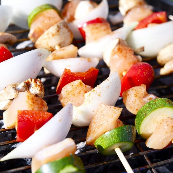 Chicken, red pepper, onion, and zucchini kebabs grilling on a barbecue.