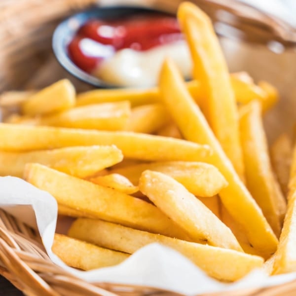 Golden french fries in a woven basket with a small dish of ketchup and mayonnaise.